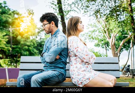 Un jeune couple contrarié assis dos à dos dans un parc, un couple malheureux assis dos à dos sur le banc. Concept de problèmes de couple et de crise. Jeune couple Banque D'Images