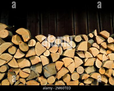 Bois de chauffage de chêne entier, fendu en deux et haché près du mur de l'ancien hangar à bois Banque D'Images