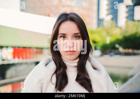 Vue avant d'une jeune femme sérieuse regardant la caméra. Gros plan portrait d'une adolescente brune debout à l'extérieur. Photo d'une jolie femme isolée avec une expression triste. Photo de haute qualité Banque D'Images