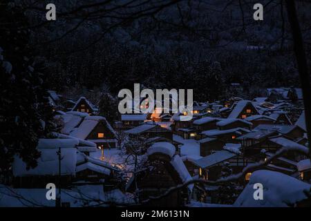 Les lumières des maisons traditionnelles brillent dans un village de montagne enneigé la nuit Banque D'Images