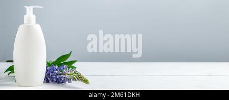 Bouteille cosmétique avec lotion et fleurs lupin sur fond gris. Cosmétiques naturels pour les soins du corps et du visage. Concept de produits spa bio, relaxati Banque D'Images