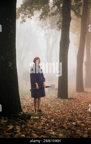 Une femme avec un parapluie se tient dans le parc par temps brumeux. Banque D'Images