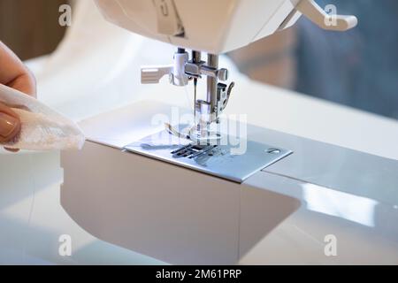 Vue rapprochée du dessus du tissu de couture des mains de femmes en machine de fabrication sur le lieu de travail. Pied de pression de l'aiguille avec fond blanc flou Banque D'Images