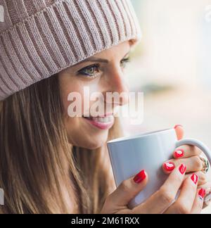 femme caucasienne avec capuchon en laine dans le profil tenant une tasse de café blanc. concept de détente et de bien-être. Banque D'Images