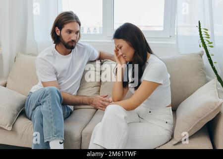 Un homme et une femme de différentes races s'assoient sur le canapé dans une pièce à la maison et parlent de leurs problèmes les uns aux autres. Un style de vie de famille sans stress Banque D'Images