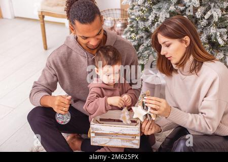 Une famille est assise tenant une boîte en bois avec des jouets de Noël. Banque D'Images