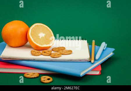 Carnets et orange sur fond vert, concept d'en-cas scolaire. Banque D'Images