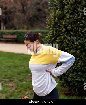 Vue latérale d'une athlète féminine positive dans un sweat-shirt coloré debout près des buissons verts avec les mains à la taille pendant l'entraînement Banque D'Images