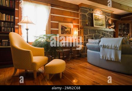 Fauteuil rembourré jaune avec pouf et dos de canapé dans le salon avec parquet en bois dur verni à l'intérieur de la maison en rondins construite en 1977. Banque D'Images