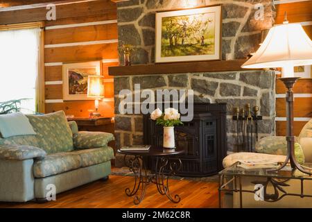 Canapés vert clair rembourrés et cheminée en pierre naturelle dans le salon avec parquet en bois franc verni à l'intérieur d'une maison en rondins construite en 1977. Banque D'Images