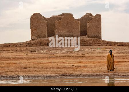 Homme dans des vêtements traditionnels debout à côté de la maison de boue abandonnée près de Tombouctou, Mali , Afrique de l'Ouest . Banque D'Images