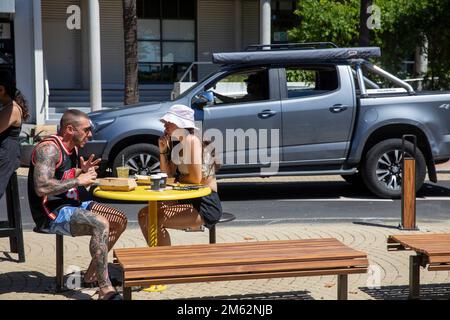 Couple dehors ayant un café à Avalon Beach café, l'homme est fortement tatoué sur le bras droit et la jambe, jeune femme n'a pas de tatouages, Sydney, NSW, Australie Banque D'Images