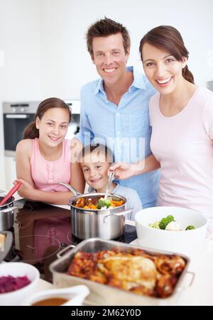 Chacun fait sa part pour faire un repas génial. Portrait d'une famille ravie de cuisiner ensemble un grand repas délicieux dans la cuisine. Banque D'Images