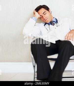 Jeune médecin fatigué dormant sur une chaise à l'hôpital. Portrait d'un jeune médecin fatigué dormant sur une chaise à l'hôpital. Banque D'Images