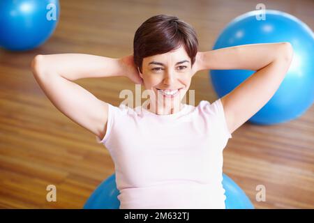 Femme faisant s'asseoir sur le ballon de sport. Femme souriante utilisant le ballon de sport et faisant des asseyez-vous pendant son entraînement. Banque D'Images