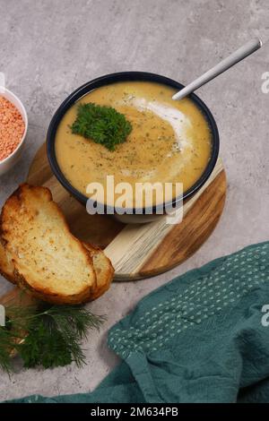 purée de soupe aux lentilles rouges dans un bol sombre avec du pain sur une table en marbre gris Banque D'Images