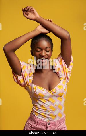 Happy African American mannequin avec eyeliner jaune dans une tenue colorée debout en studio Banque D'Images