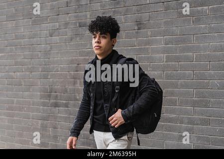 Originaire du Venezuela, 22 ans d'Amérique latine, avec cheveux bouclés et sac à dos debout contre un mur en briques grises Banque D'Images