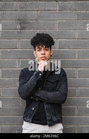 Portrait d'un jeune homme rétif ethnique aux cheveux bouclés dans une tenue décontractée debout regardant l'appareil photo Banque D'Images