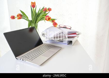 Bureau blanc avec ordinateur portable, documents et un bouquet de tulipes rouges, concept pour les affaires à domicile ou l'étude, espace de copie, foyer sélectionné, profondeur étroite de Banque D'Images