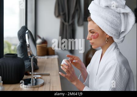 Jeune femme appliquant le patch de beauté sous les yeux après avoir pris le bain Banque D'Images