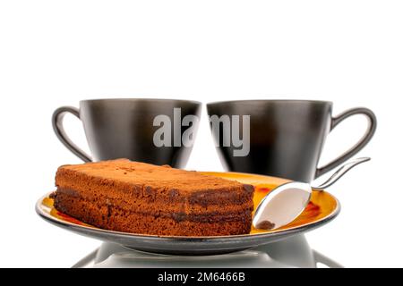 Un morceau de gâteau à la truffe sur une soucoupe en céramique avec deux tasses noires, macro, isolé sur fond blanc. Banque D'Images