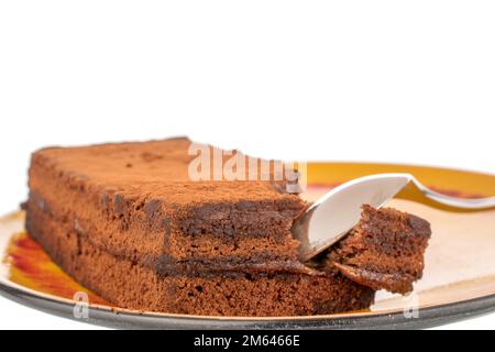 Un morceau de gâteau à la truffe sur une soucoupe en céramique avec une cuillère en métal, macro, isolée sur fond blanc. Banque D'Images