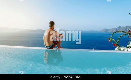 Santorini Grèce Oia, jeunes hommes en short de bain se détendre dans la piscine donnant sur la caldeira de l'île de Santorini Grèce, piscine à débordement, un jeune homme sur des vacances de luxe en Europe Grèce Banque D'Images