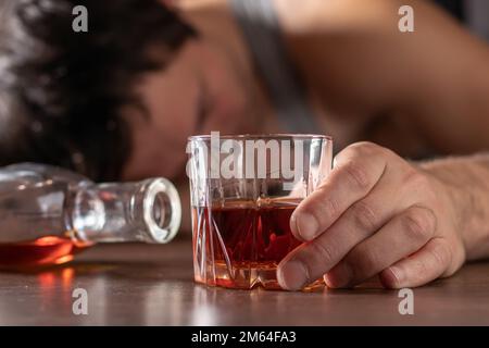 Alcoolisme, dépendance à l'alcool et concept de personnes - homme alcoolique avec un verre de whisky couché ou endormi sur table. Banque D'Images