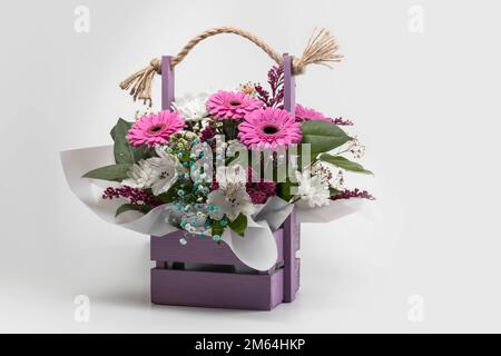 Beau bouquet de fleurs lumineuses dans un panier en bois sur fond blanc. Banque D'Images