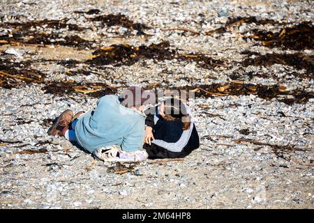 Portreath,Cornouailles,2nd janvier 2023,Un jeune couple se trouve sur la plage à marée haute à Portreath, Cornouailles. Le ciel était bleu avec le soleil glorieux et 8C, la prévision après aujourd'hui est pour le temps humide pour les prochains jours. Le pétrolier Maersk Bering a été ancré juste au large de la côte, ce qui est très inhabituel.Credit: Keith Larby/Alamy Live News Banque D'Images