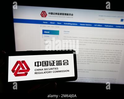 Personne possédant un smartphone avec le logo de la Commission chinoise de réglementation des valeurs mobilières (CPCR) à l'écran devant le site Web. Mise au point sur l'affichage du téléphone. Banque D'Images