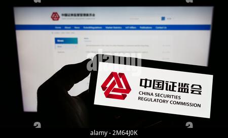 Personne tenant un téléphone portable avec le logo de la Commission chinoise de réglementation des valeurs mobilières (CSRC) à l'écran en face de la page Web. Mise au point sur l'affichage du téléphone. Banque D'Images