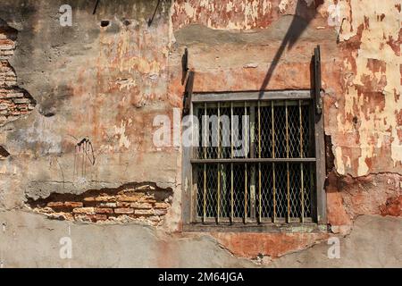 Une fenêtre avec des grilles métalliques sur un mur de briques en ruines rompues dans la vieille ville de George Town à Penang, Malaisie. Banque D'Images