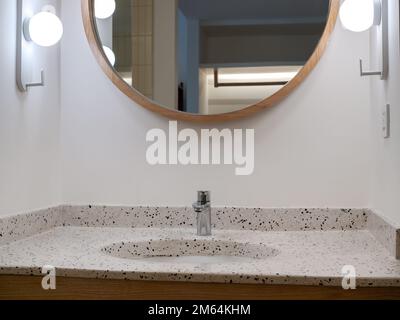 Robinet ou robinet en acier inoxydable chromé argent en forme ronde de carreaux de terrazzo décoration de lavabo avec miroir rond et lampes sur bac mural blanc Banque D'Images