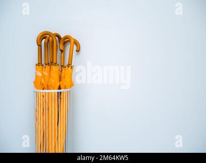 De nombreux parasols jaunes avec poignée en bois stockés dans le stockage de parapluie blanc en acier vintage isolé sur fond de mur blanc avec espace de copie. Banque D'Images