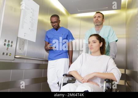 infirmière attentionnés poussant le patient en fauteuil roulant à l'ascenseur de l'hôpital Banque D'Images