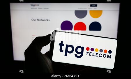 Personne tenant un téléphone portable avec le logo de la société australienne TPG Telecom Limited à l'écran devant la page Web d'affaires. Mise au point sur l'affichage du téléphone. Banque D'Images