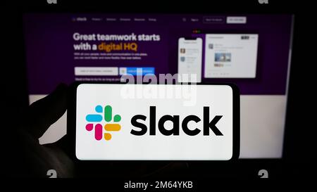 Personne tenant un smartphone avec le logo de la société logicielle américaine Slack technologies LLC sur l'écran devant le site Web. Mise au point sur l'affichage du téléphone. Banque D'Images