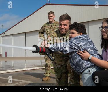 Grayson 'Blazin' Anthony, pilote de l'escadre de chasse 138th pour une journée, et le chasseur d'incendie de l'escadron d'ingénieurs civils 138th, Airman Cody Steever, vaporise de l'eau à partir d'un tuyau d'incendie 2 avril 2022 à la base de la Garde nationale aérienne de Tulsa, en Oklahoma. La visite du service des incendies a été la partie préférée de Grayson dans le programme pilote pour Une journée. Banque D'Images