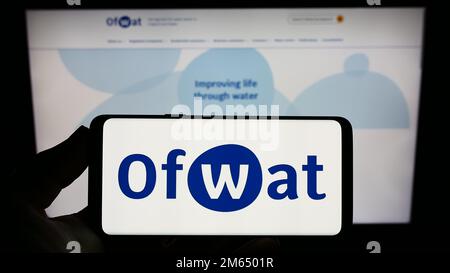 Personne tenant un smartphone avec le logo de l'autorité de régulation des services d'eau (Ofwat) sur l'écran devant le site Web. Mise au point sur l'affichage du téléphone. Banque D'Images