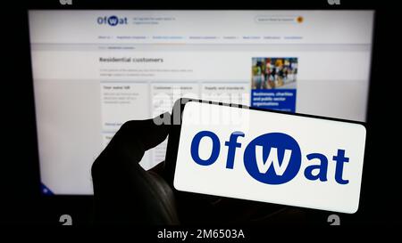 Personne tenant un téléphone portable portant le logo de l'autorité de régulation des services d'eau (Ofwat) à l'écran devant la page Web. Mise au point sur l'affichage du téléphone. Banque D'Images