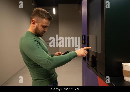 Un homme de race blanche choisit le café dans une machine en libre-service. Banque D'Images