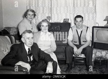 1950s, historique, vie familiale dans la Grande-Bretagne d'après-guerre, différentes générations d'une famille assise dans une salle de réception pour leur photo, un jeune homme, sa mère et grands-parents, un petit ensemble de télévision de l'époque est assis sur une table à l'angle, Angleterre, Royaume-Uni. Banque D'Images