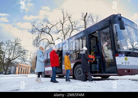 Les personnes attendant et entrant dans les transports publics nécessaires. Vieil homme en manteau rouge deux femmes en vestes noires et bleues et garçon portant un anorak jaune debout i Banque D'Images