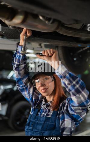 Une mécanique femelle dévisser les écrous sur le bas de la voiture qui se trouve sur le pont élévateur. Une fille au travail d'un homme. Banque D'Images