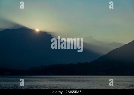 lever du soleil sur le lac de côme avec des rayons de soleil qui brillent à travers les vallées de montagne et le soleil se montrant juste au-dessus de la montagne Banque D'Images