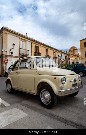 Une photo verticale d'une Fiat 500 couleur crème garée dans une rue calme d'une ville Banque D'Images
