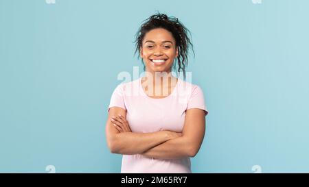 Portrait d'une femme afro-américaine heureuse debout avec les bras pliés, regardant et souriant à l'appareil photo, fond bleu Banque D'Images