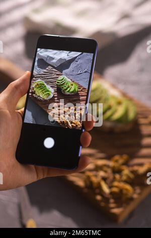 Smartphone prenant des photos de sandwichs biologiques sains avec de l'avocat. Main d'homme. Banque D'Images